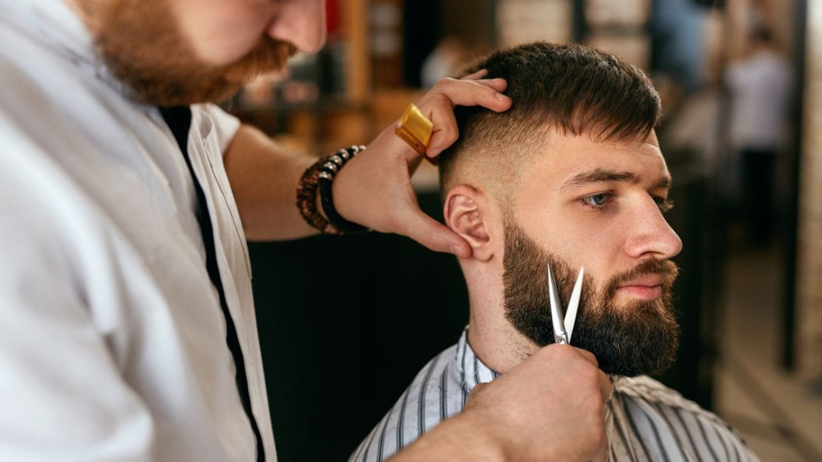 Barbeiro fazendo a barba de um homem com a tesoura - Software para Barbearia